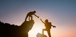 Two people rock climbing and one person leaning down to assist their climbing partner